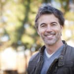 A man smiling in front of a tree.