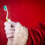 Santa claus holding a toothbrush on a red background.