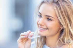 Invisalign orthodontics concept - Young attractive woman holding - using invisible braces or trainer.